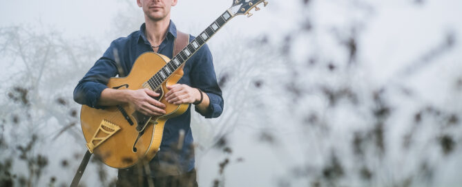 Christian Bekmulin Jazzgitarrist - Musikerporträt für Website und Presse, mit Jazzgitarre steht Bekmulin in nebliger Natur und blickt ruhig in die Kamera.