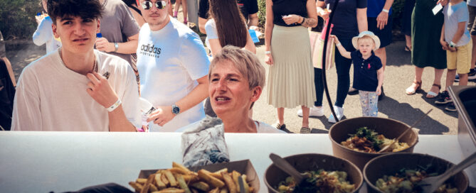 Menschen bestellen Essen an einem Foodtruck im Freien bei sonnigem Wetter.