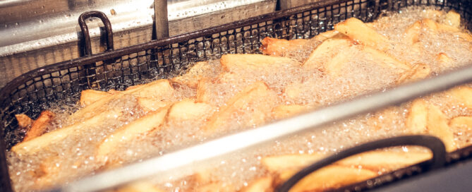 Fritten frittieren in Metallkörben mit sprudelndem Öl in einer Gewerbeküche.