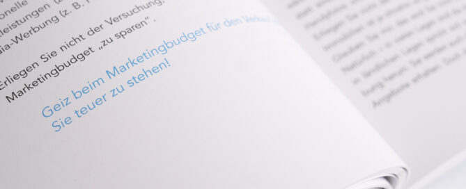 Offenes deutsches Buch mit blau markiertem Text auf weißer Seite in Nahaufnahme.