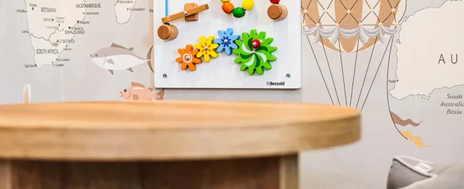 Kinderleseecke mit Weltkarten-Wandbild, Holzspielzeug, Buch „Der Bär im Büro“ und Sternkissen.