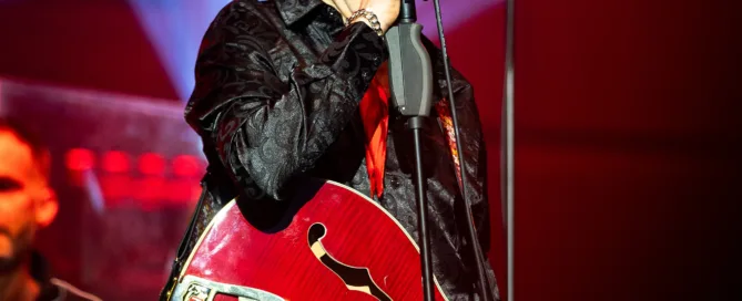 Musiker mit roter E-Gitarre singt leidenschaftlich live bei Konzert in Frankfurt.