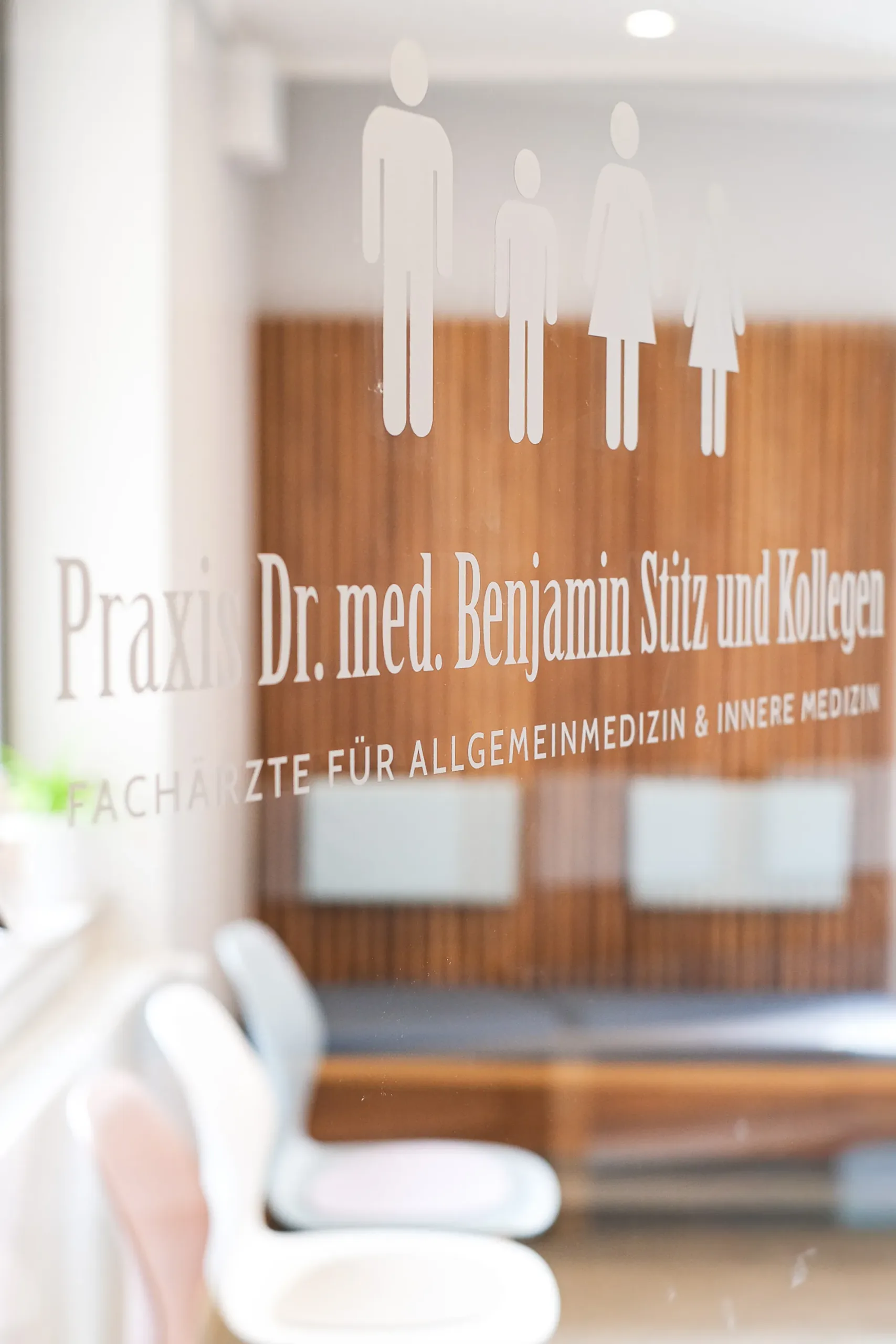Eingang einer Arztpraxis für Allgemeinmedizin in Deutschland Glaswand einer Arztpraxis mit Aufschrift „Praxis Dr. med. Benjamin Stitz und Kollegen“ und Familienpiktogrammen.
