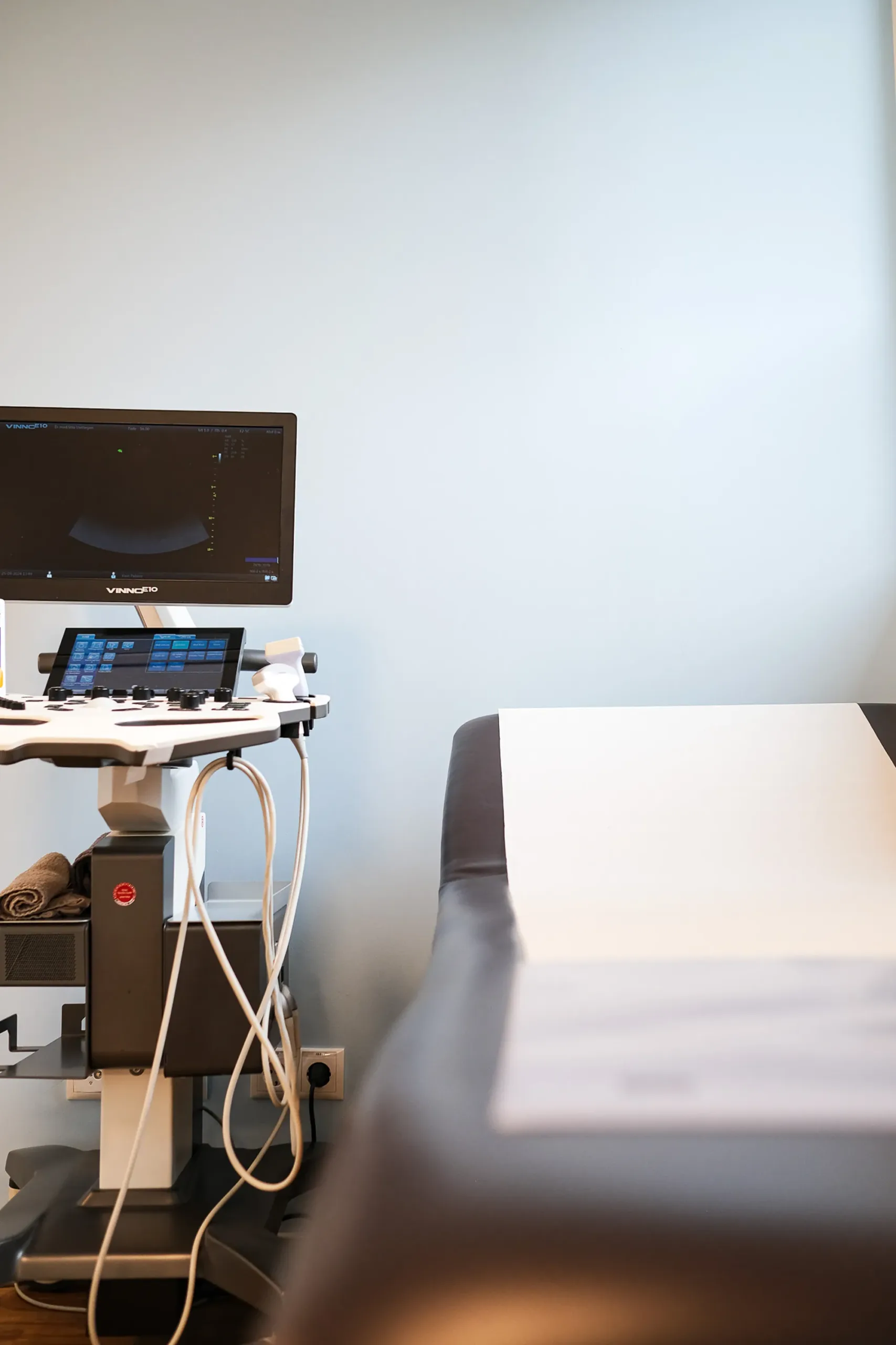 Ultraschallgerät und Untersuchungsliege im modernen Behandlungsraum Ultraschallgerät neben Untersuchungsliege in sauberem, modernem Behandlungsraum.