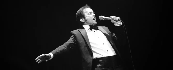 Sänger im Anzug performt mit Mikrofon auf beleuchteter Bühne mit Band im Barocktheater Schwetzingen.