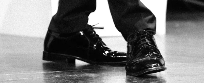 Schwarz-weiß Foto von eleganten, glänzenden Herrenschuhen auf einer Bühnenfläche in Nahaufnahme.