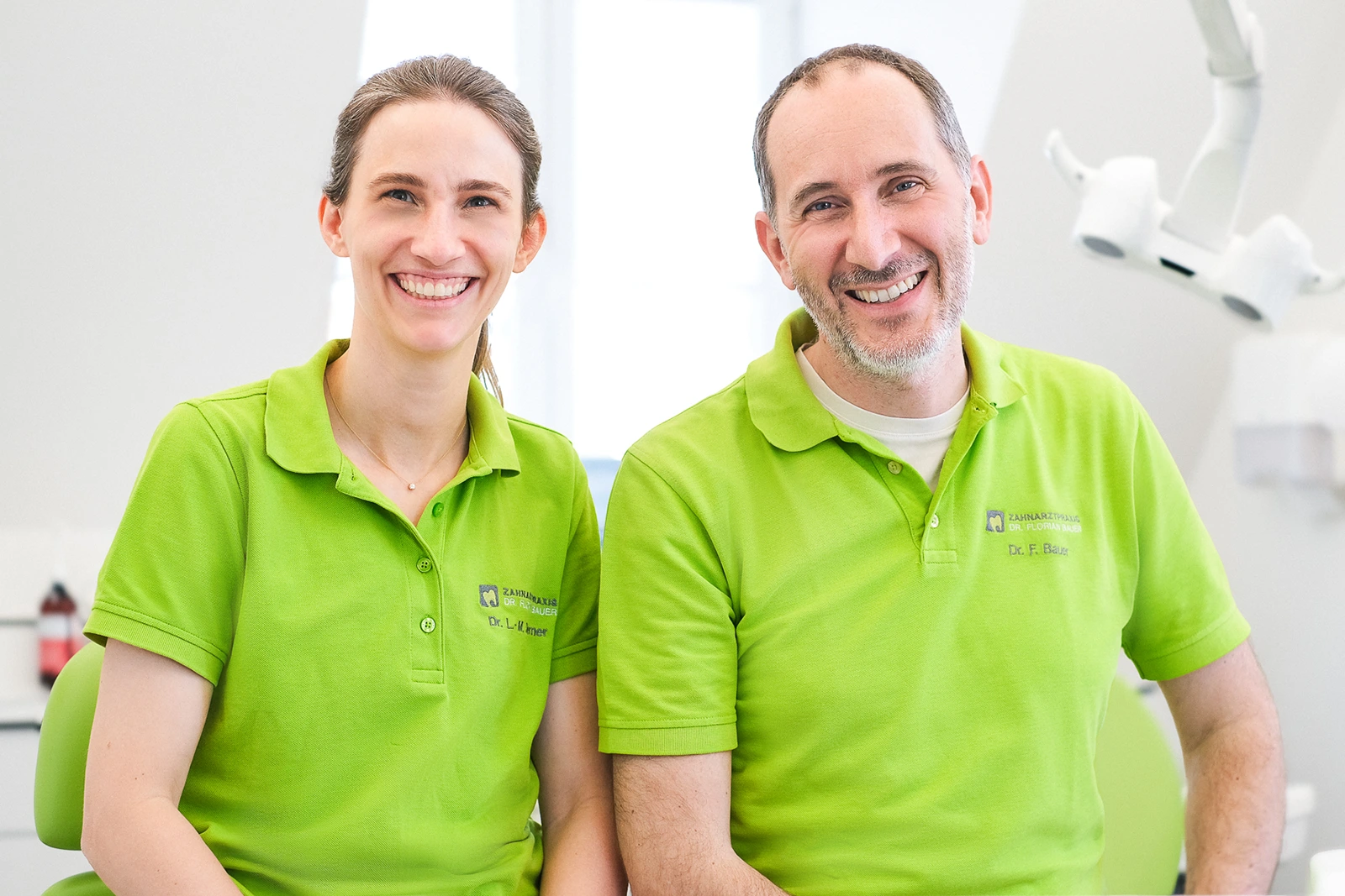 Freundliches Dental Team in moderner Praxis in Würzburg Zwei Zahnärzte in grünen Polohemden in modernem Behandlungsraum in Würzburg.