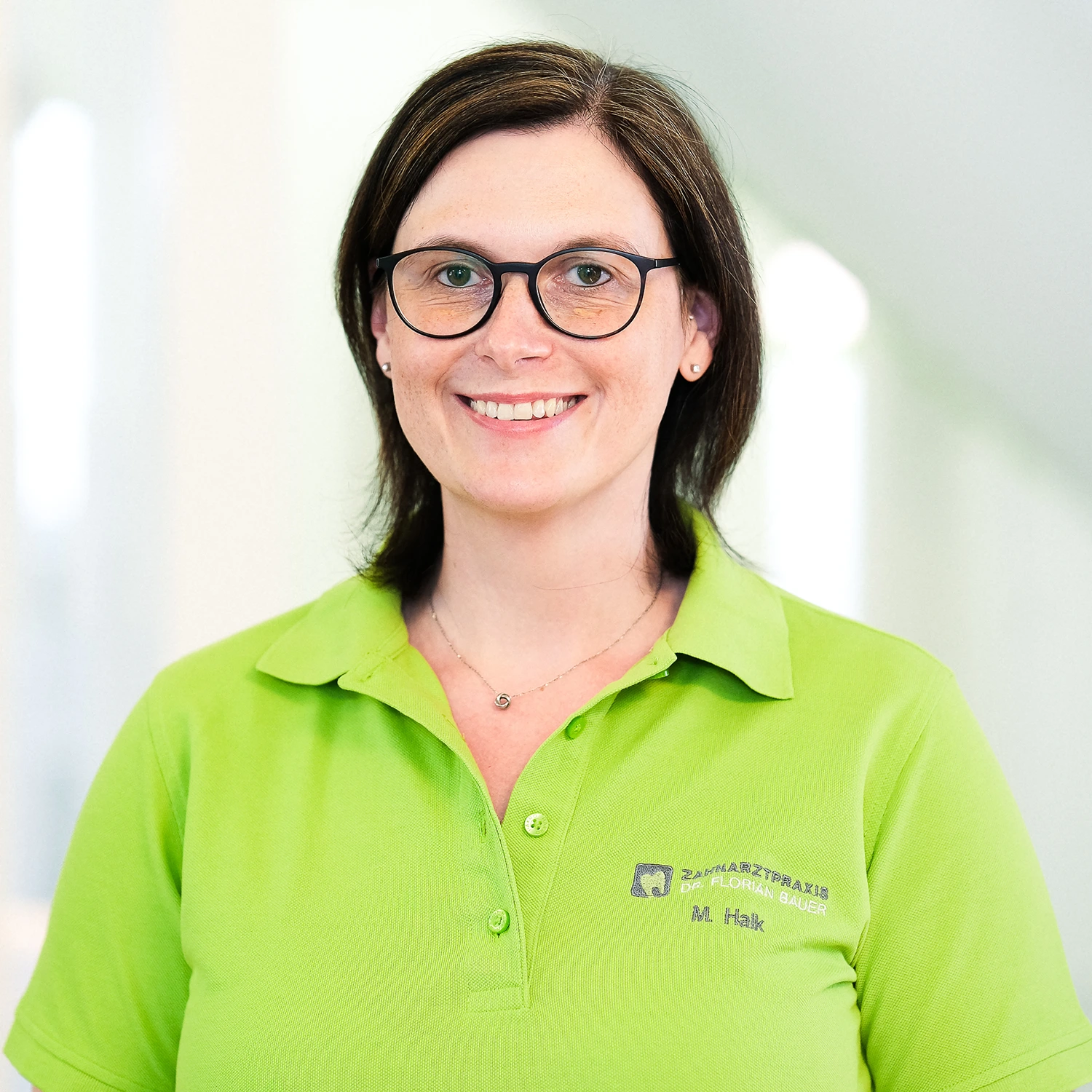 Professionelles Praxisporträt einer freundlichen Mitarbeiterin Freundliche Frau in grünem Polo mit Brille, professionelles Portrait in Praxis-Umfeld, Wurzburg.