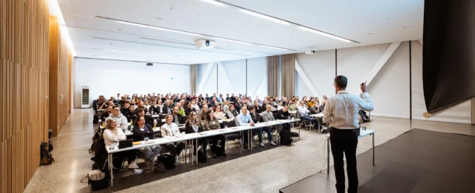 Moderator bei modernem Business-Event in Würzburg, hält Präsentation vor engagiertem Publikum.