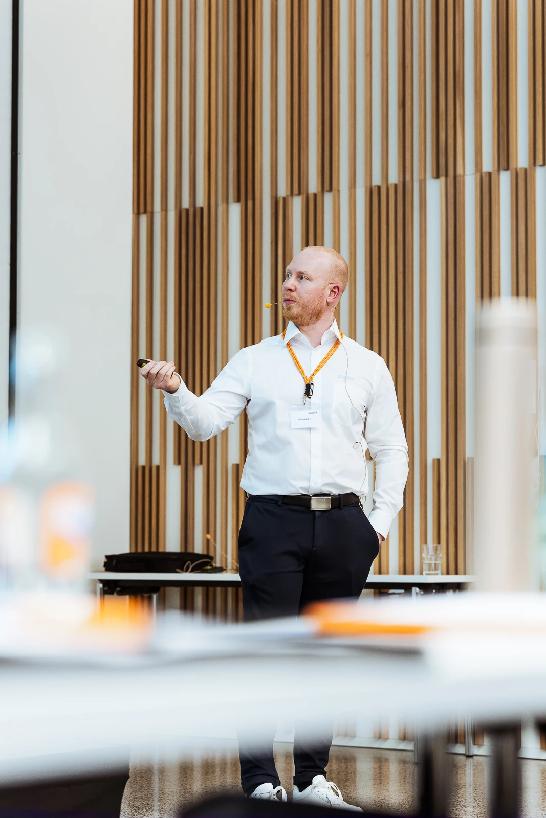 Professioneller Redner bei Business-Veranstaltung in Würzburg Mann hält Präsentation bei Business-Event in Würzburg, trägt weiße Hemd, dunkle Hose, Lanyard, gestikuliert.