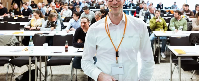 Mann beim Business-Event in Würzburg, spricht mit Teilnehmern vor einem Konferenzraum.