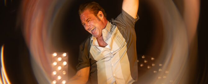 Dick Brave bei Live-Konzert in Frankfurt, umgeben von pulsierenden Lichtstrahlen und dynamischer Energie.