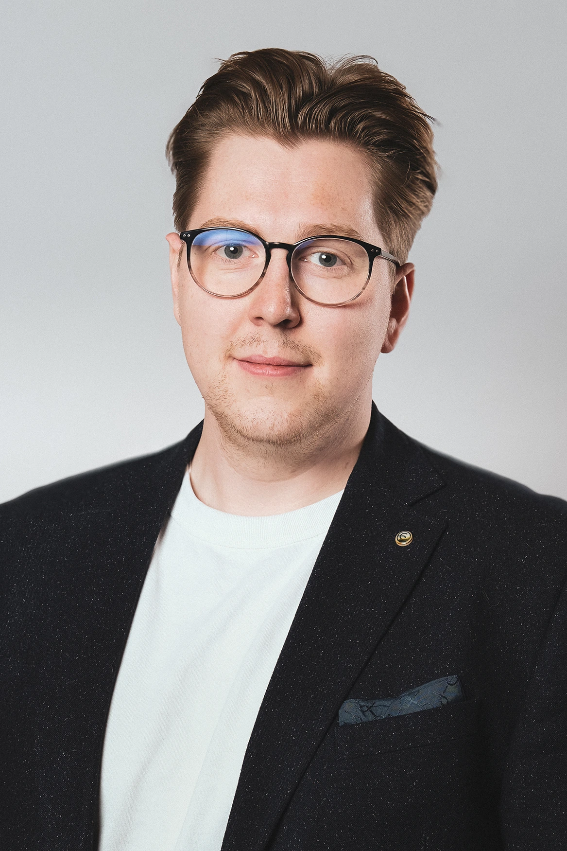 Professionelles Businessportrait eines jungen Mannes in formeller Kleidung mit Brille, neutralem Hintergrund.