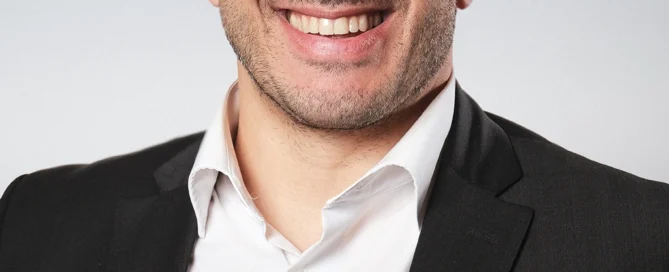 Professionelles Businessportrait eines Mannes in Anzug und Brille vor neutralem Hintergrund.