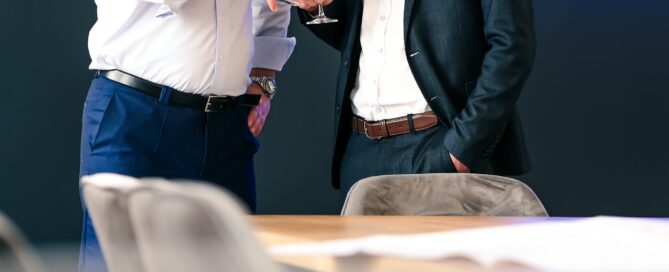 Zwei Männer feiern im modernen Büro von Immo Heller mit Sektgläsern, Neon-Schild im Hintergrund, professionelles Business-Setting.