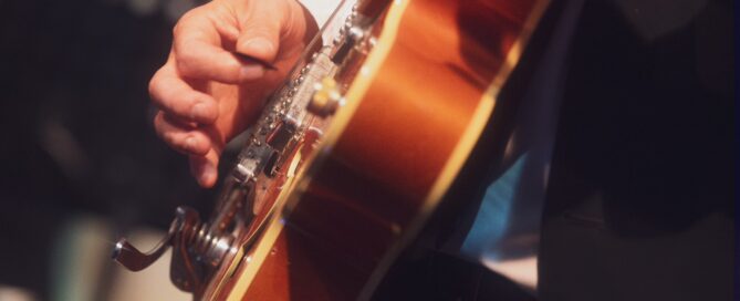 Musikerhand beim Solospiel auf einer edlen, amberfarbenen Hollonegitarre, im formellen Rahmen in Würzburg.