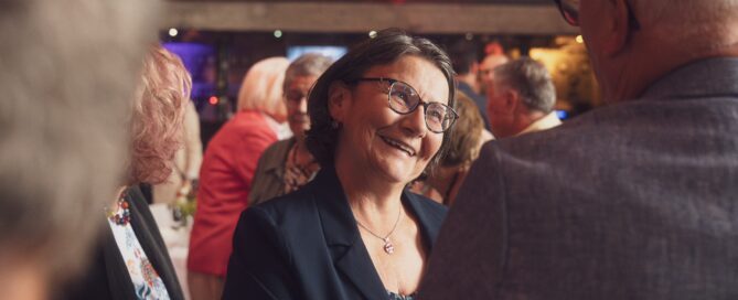 Frau mit Brille und dunklem Blazer lächelt bei einer festlichen Veranstaltung in Würzburg.