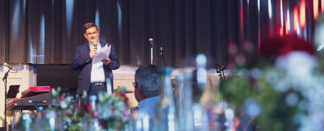 Gesprochener Redner bei formellem Event in eleganter, festlich dekorierter Halle in Würzburg.