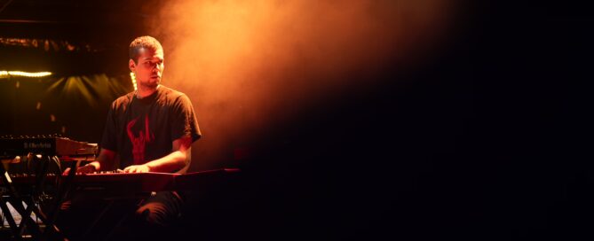 Keyboarder beim Hafensommer-Konzert in Würzburg, umgeben von orange beleuchtetem Bühnennebel.