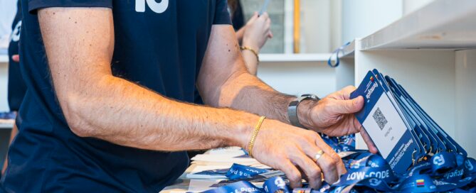 Mann sortiert blaue Lanyards und Namensschilder auf einem Tisch bei einer Konferenz in Würzburg.
